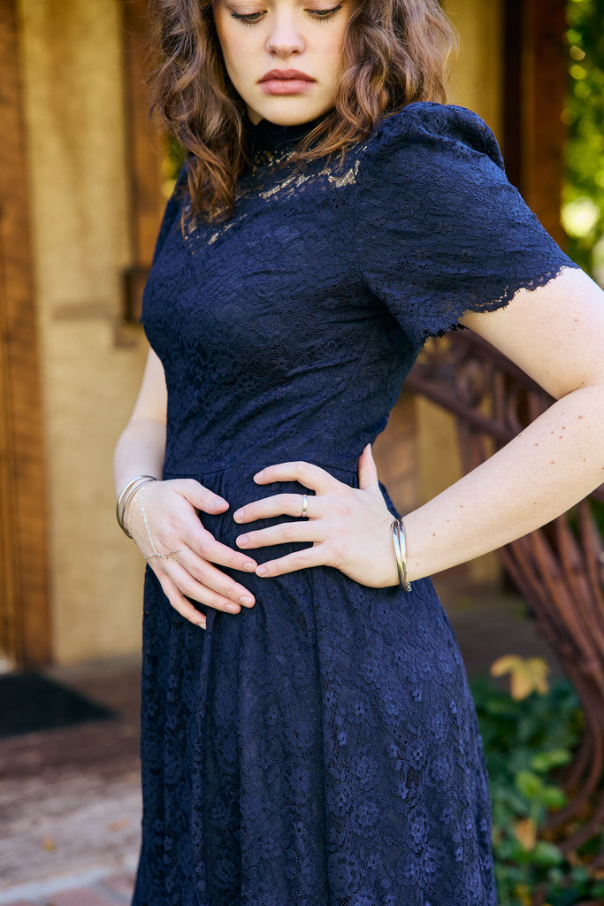 Woman wearing a navy lace dress with a blurred background - navy lace midi elegant romantic bridal shower church wedding guest outfit modest