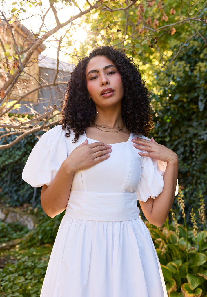 Woman in a white dress standing outdoors with greenery in the background - cotton puff sleeve white