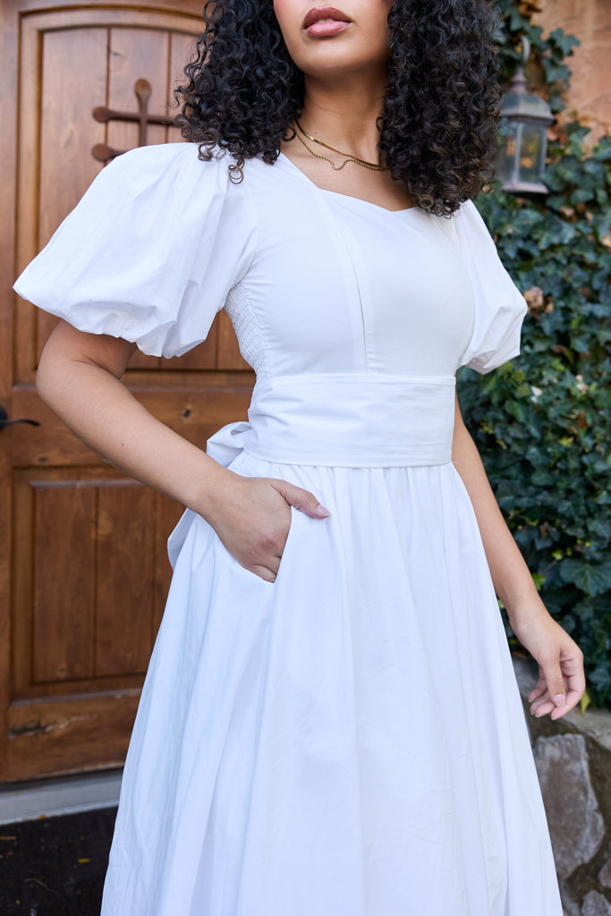 Woman wearing a white dress with puffed sleeves in front of a wooden door - cotton puff sleeve white