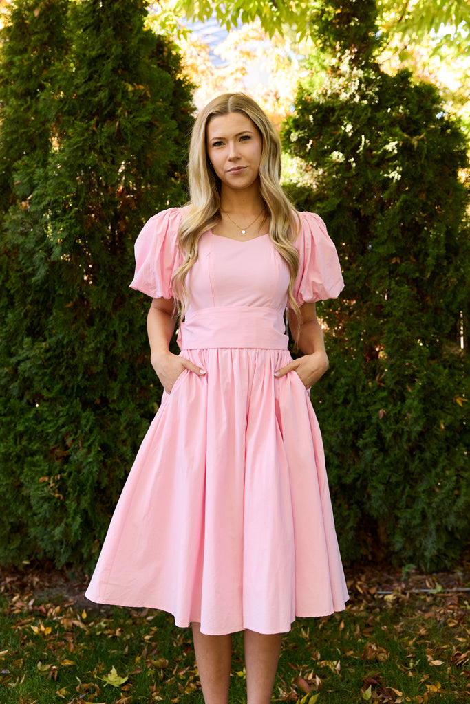 Woman wearing a pink dress standing outdoors with greenery in the background - modest cotton knee-length dress nursing-friendly