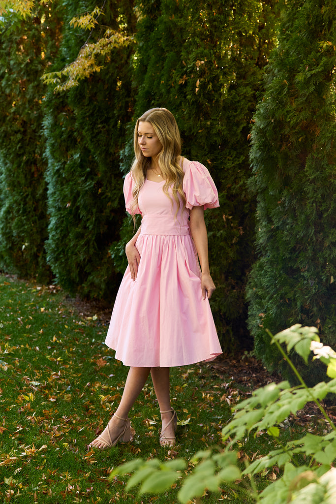 Woman in a pink dress standing in a garden with greenery - modest cotton knee-length dress nursing-friendly
