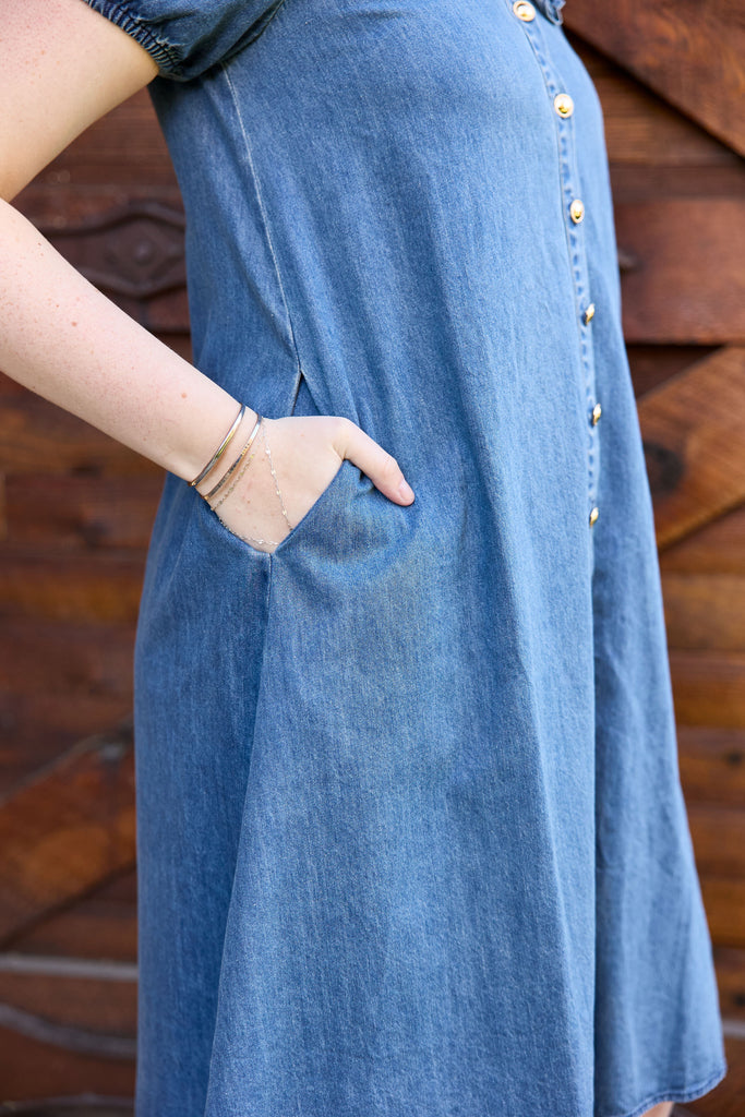 Blue denim dress with gold buttons on a wooden background - blue denim midi button down collared casual summer everyday jean picnic outfit modest