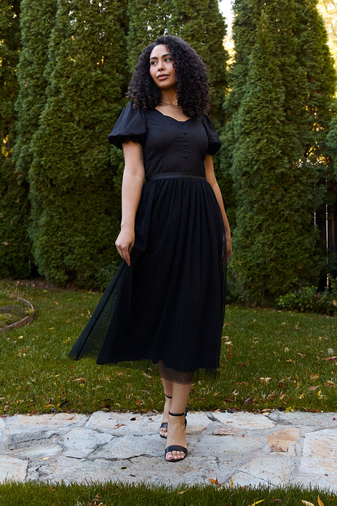 Woman in a black dress standing outdoors with green trees in the background - black ballerina modest evening cocktail wedding guest