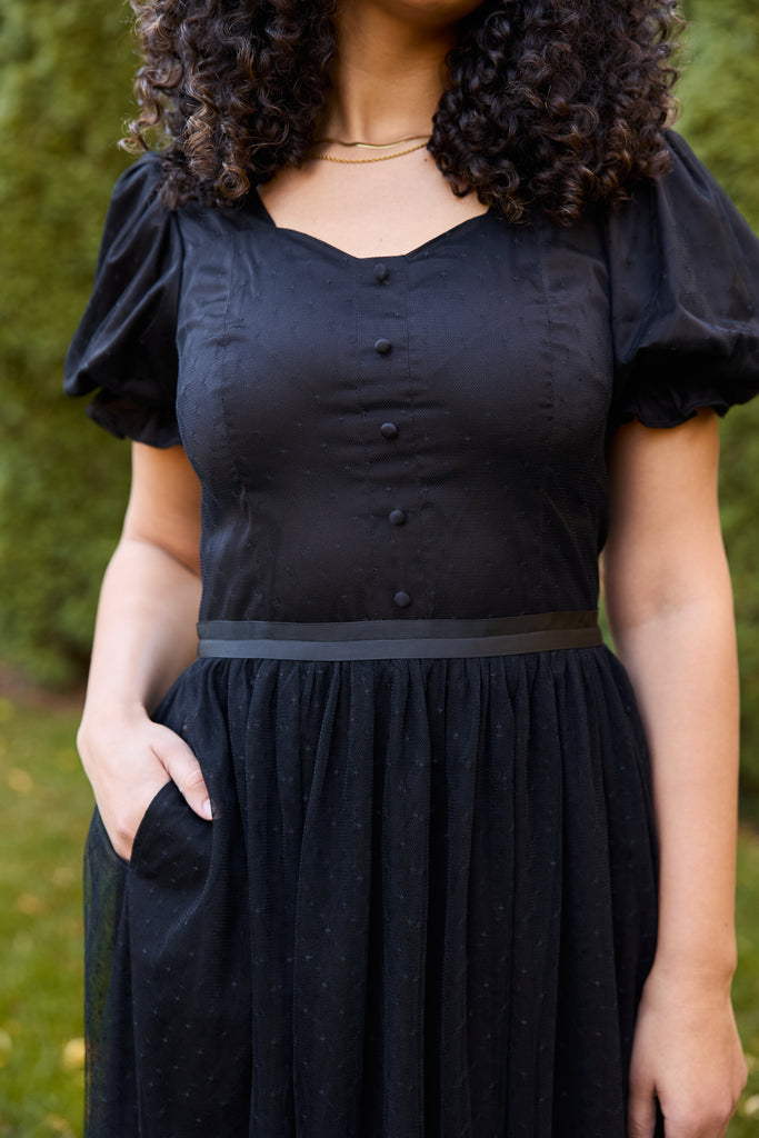 Woman wearing a black dress with puffed sleeves against a green background - black ballerina modest evening cocktail wedding guest